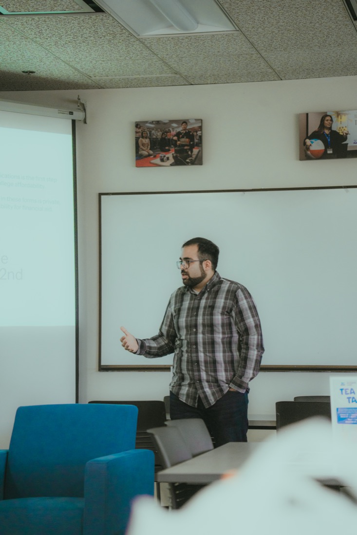 A presenter in a plaid shirt speaking in front of a whiteboard during a fellowship session