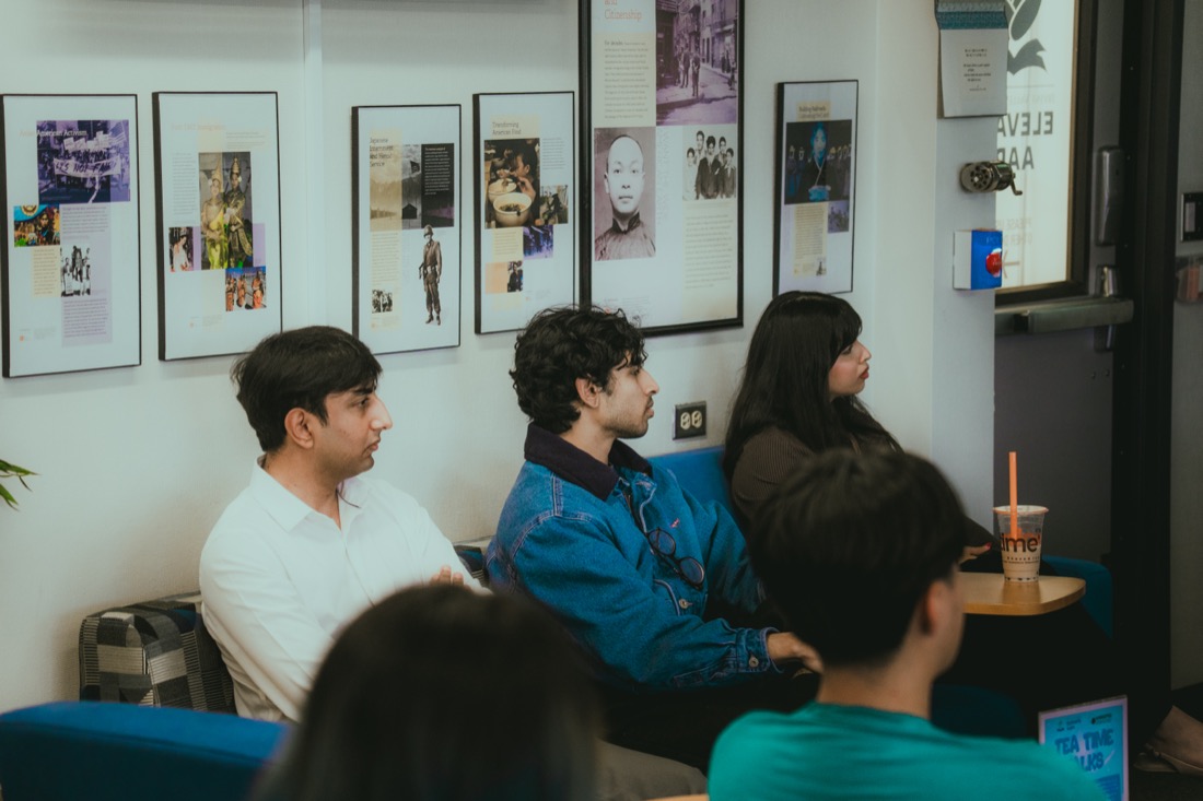 Fellows seated and listening to a presentation, with framed history posters on the wall behind them